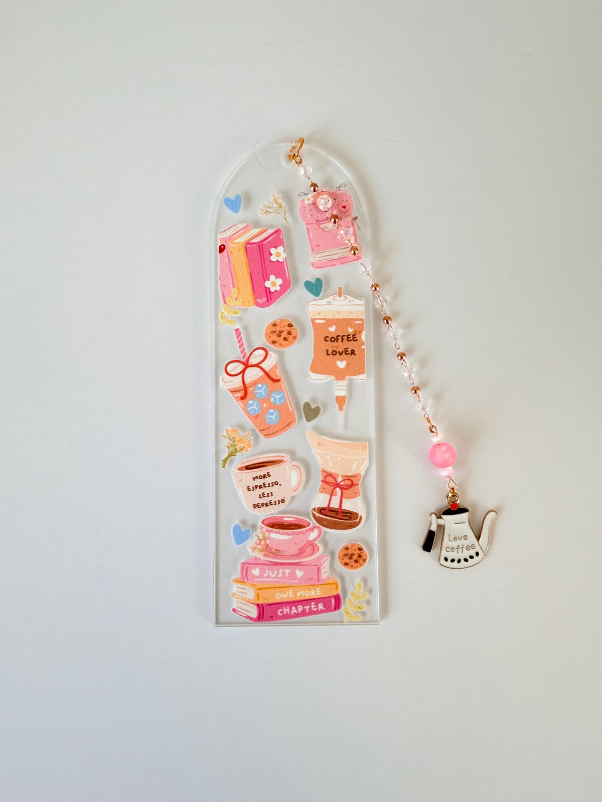 A clear acrylic bookmark decorated with cute coffee-themed designs, including a coffee cup, mug, book, and small charm, shown against a plain white  background.