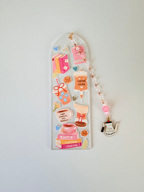 A clear acrylic bookmark decorated with cute coffee-themed designs, including a coffee cup, mug, book, and small charm, shown against a plain white  background.