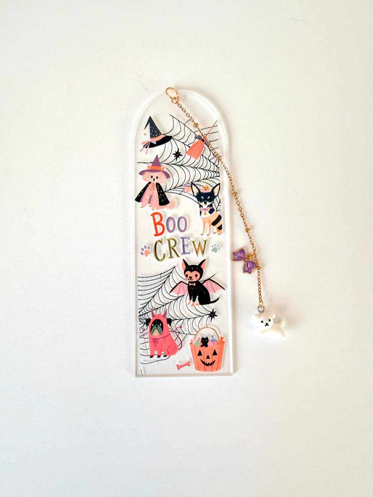 A Halloween-themed clear acrylic wall plaque featuring cartoon illustrations of witches, cats, bats, a ghost, a pumpkin, and the words 'BOO CREW'. A gold-tone hanging chain with a small white ghost charm and purple star accent hangs from the top of the plaque against a plain white wall.