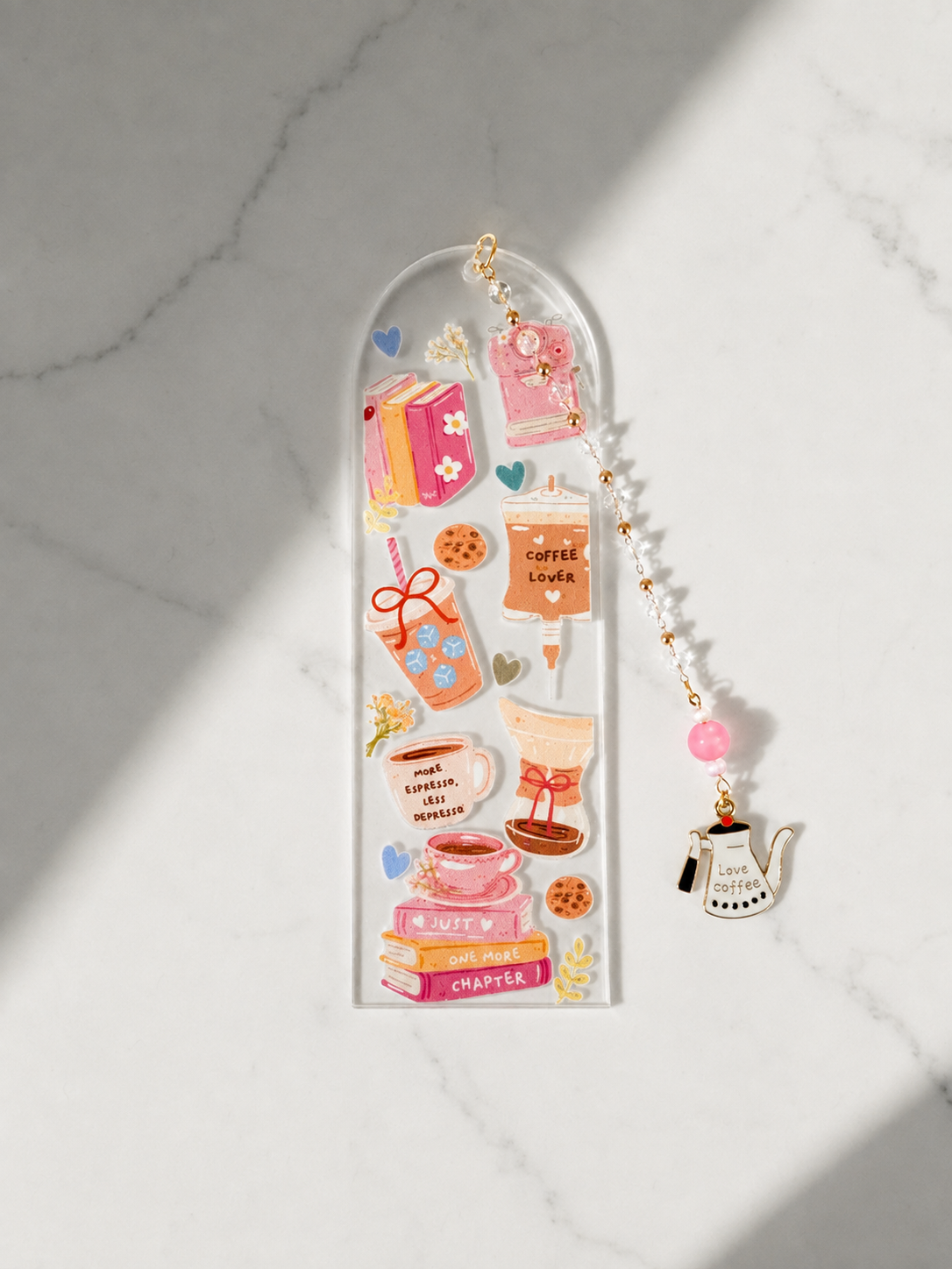 A clear acrylic bookmark with an arched top and a dangling charm, decorated with colorful coffee-themed illustrations and text, displayed on a white marble surface with soft diagonal shadows.