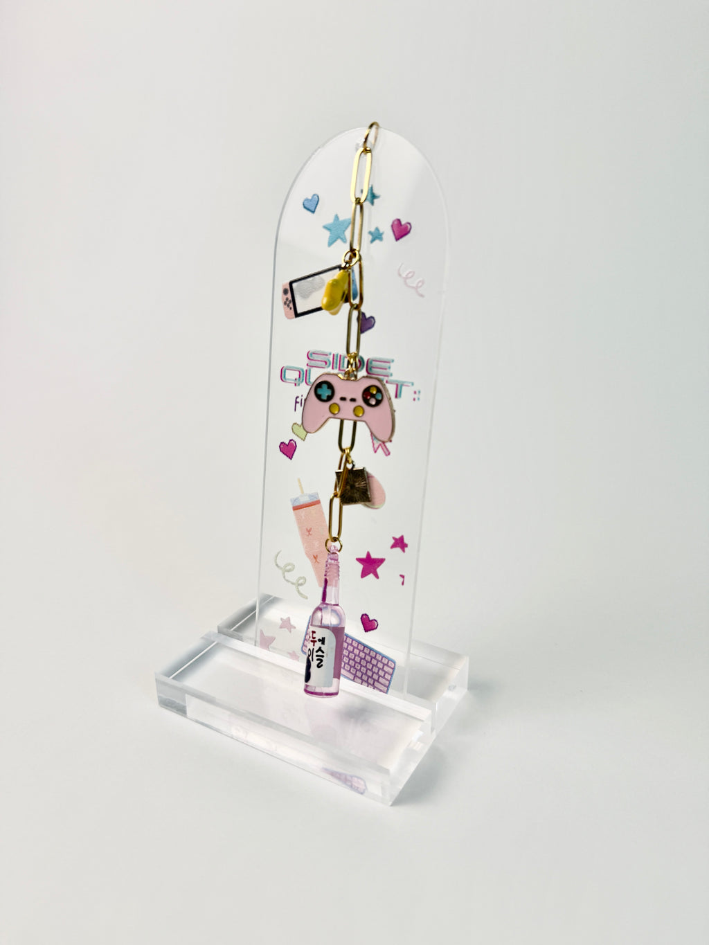arched clear acrylic bookmark with charms that have game console, yellow star, drink bottle. The bookmark has keyboard, game console and tumbler with peach and pink color aesthetics standing on white background.