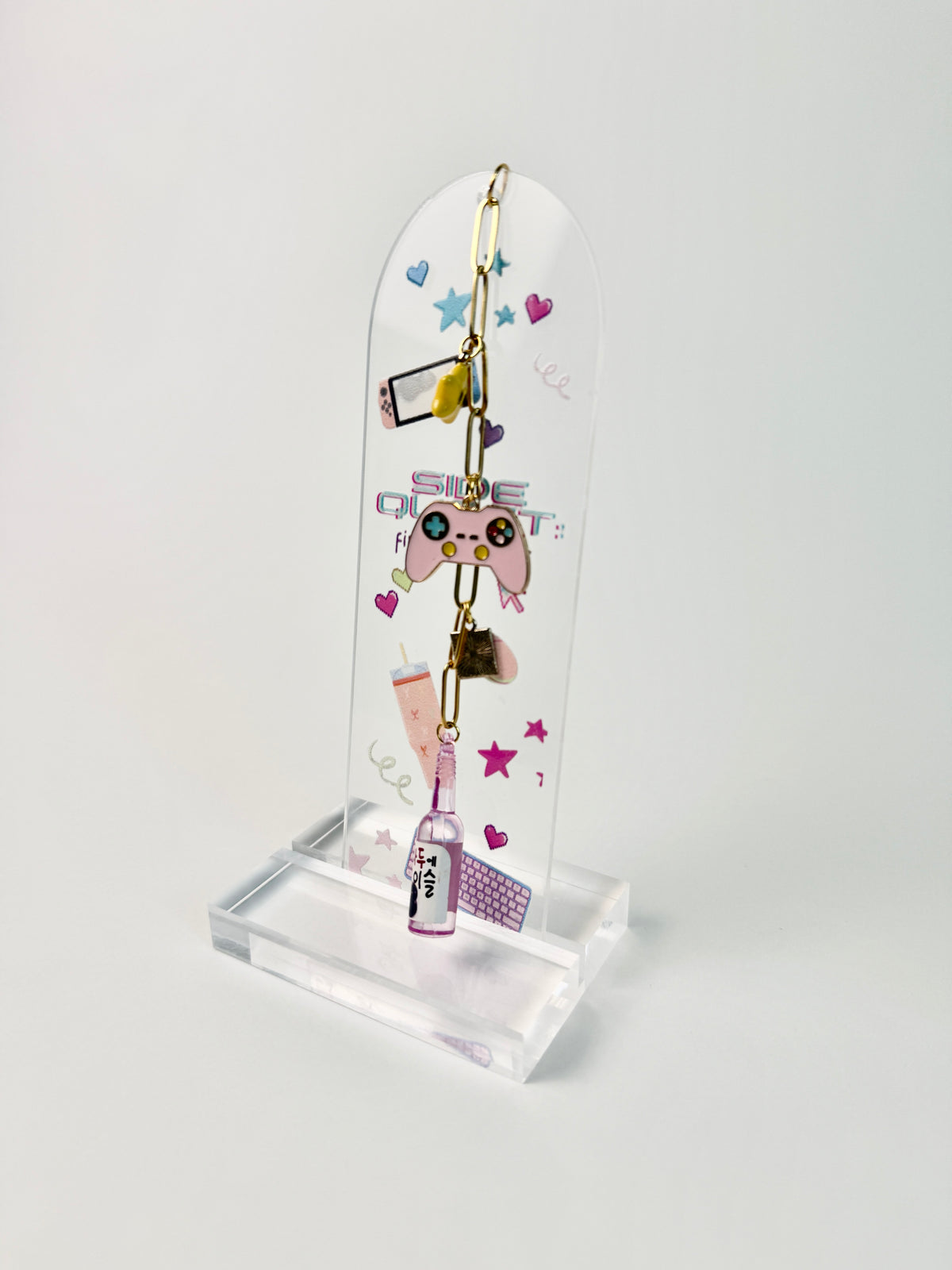 arched clear acrylic bookmark with charms that have game console, yellow star, drink bottle. The bookmark has keyboard, game console and tumbler with peach and pink color aesthetics standing on white background.