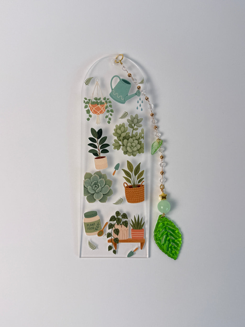 arched clear acrylic bookmark with green leaf charm. has succulents, plants, and leafs for designs on a black white background.