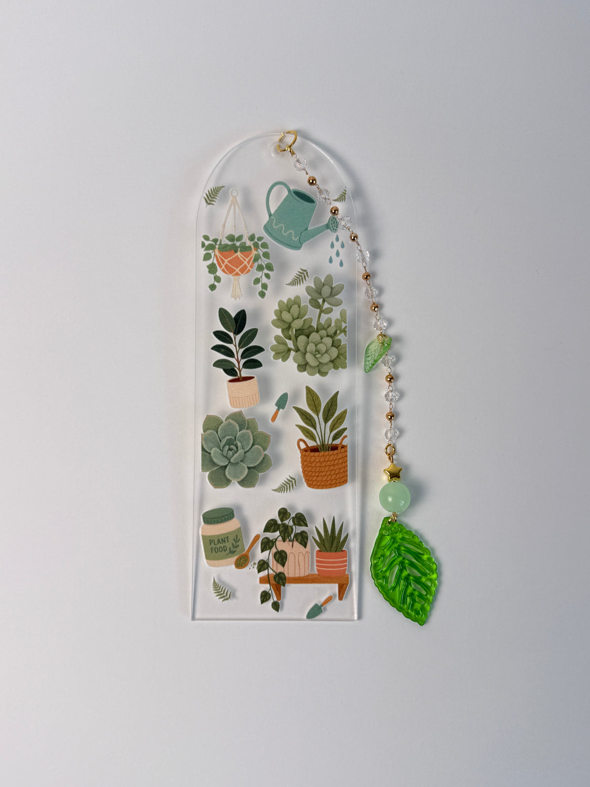 arched clear acrylic bookmark with green leaf charm. has succulents, plants, and leafs for designs on a black white background.