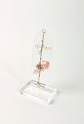 Clear arched acrylic bookmark with Sagittarius zodiac lettering, constellation artwork, an archer symbol with pink botanical details, the quote “A spirit chasing stories beyond the horizon,” and dangling star and Sagittarius heart charms. standing on white background