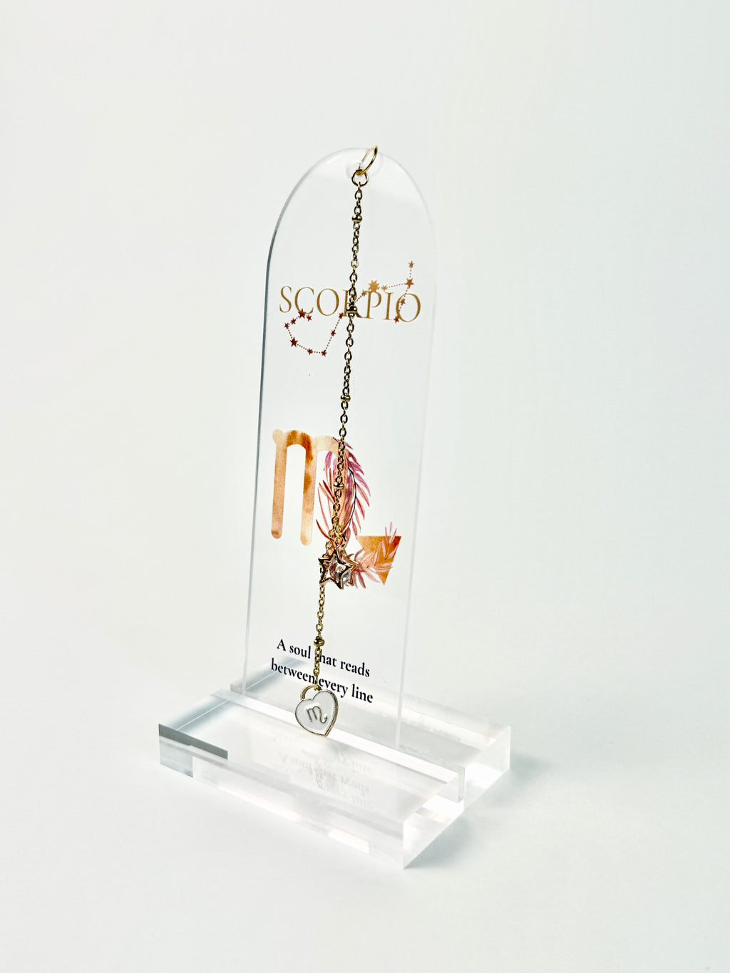 Clear acrylic Scorpio bookmark with constellation artwork and “A soul that reads between every line” lettering, finished with a gold-tone chain and white heart charm. standing acrylic holder on white background