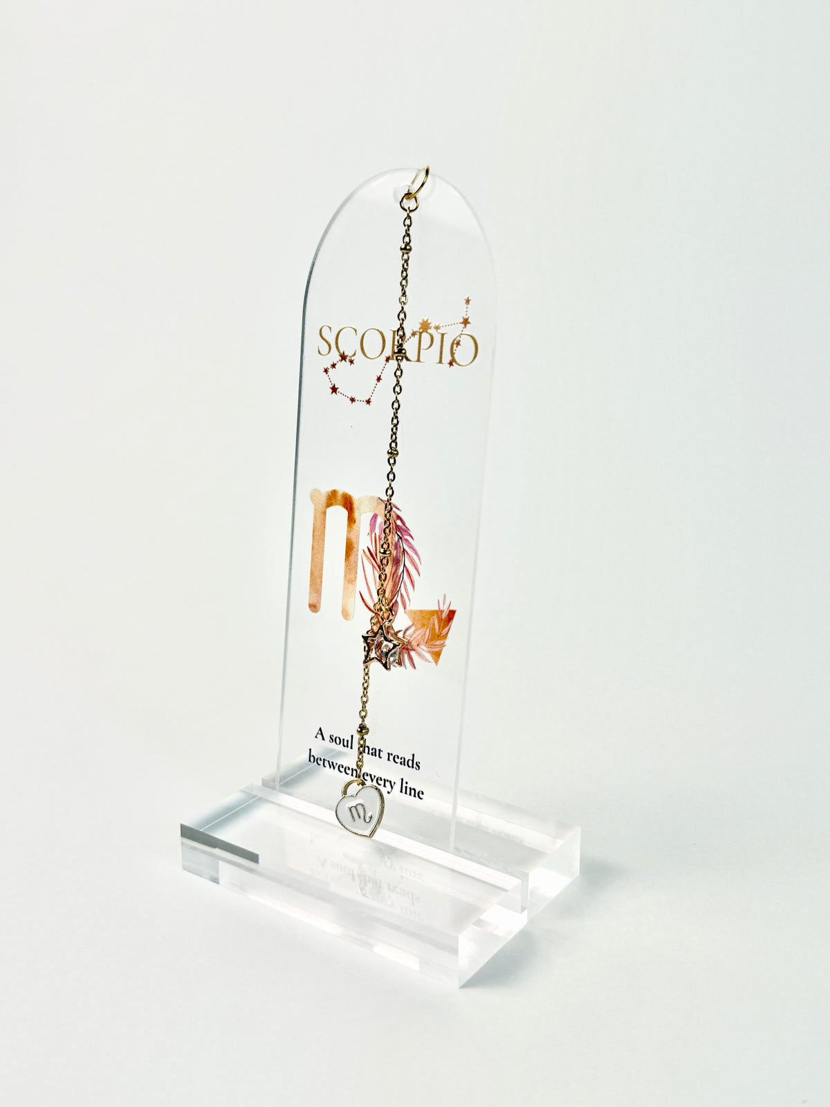 Clear acrylic Scorpio bookmark with constellation artwork and “A soul that reads between every line” lettering, finished with a gold-tone chain and white heart charm. standing acrylic holder on white background