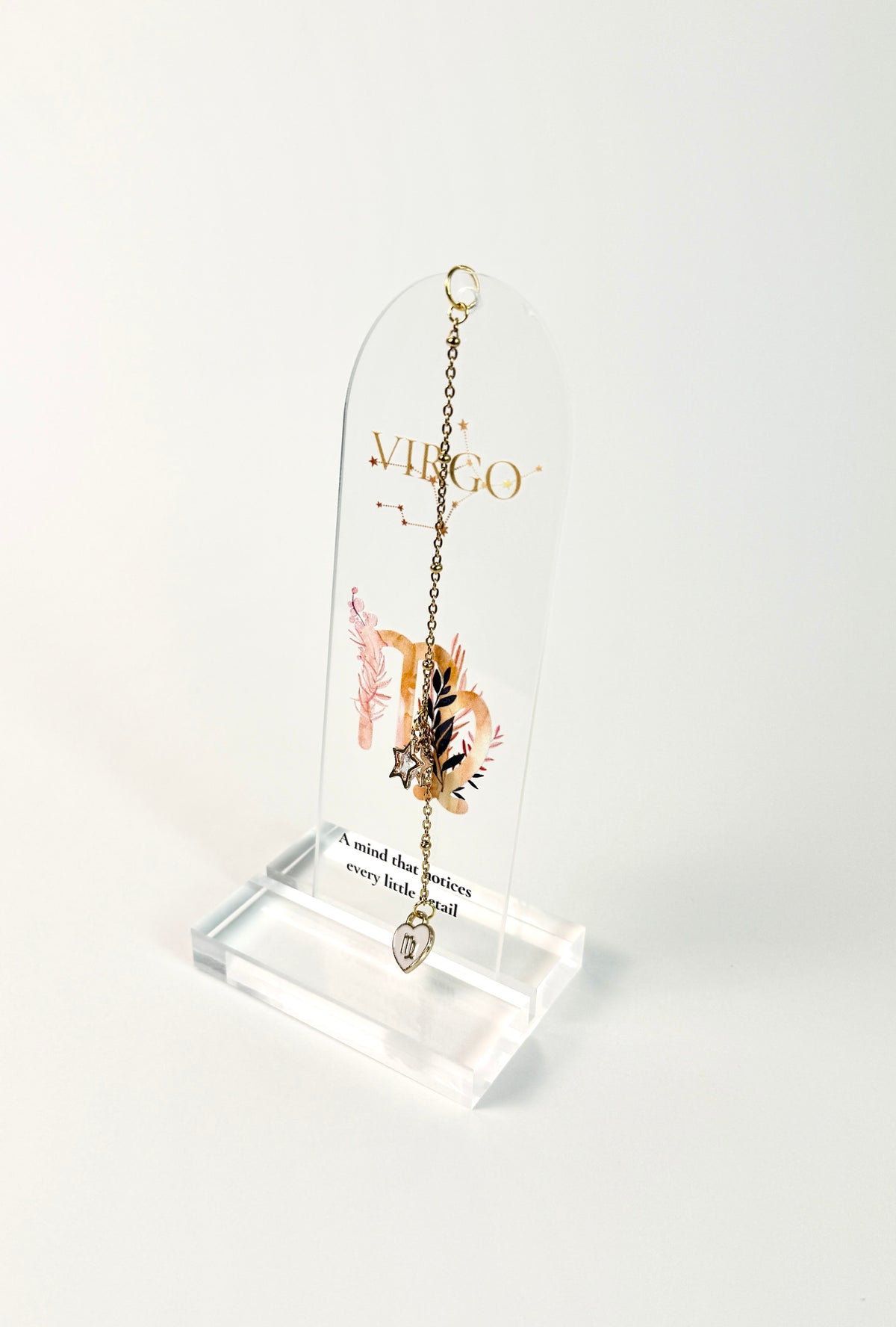 Clear arched acrylic bookmark standing on white background with Virgo zodiac lettering, constellation artwork, botanical details, the quote “A mind that notices every little detail,” and dangling star and Virgo heart charms.